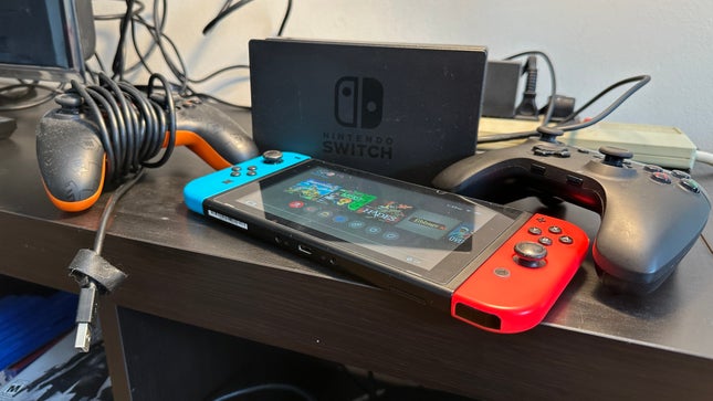 Nintendo Switch game console on the TV cabinet, surrounded by controllers and Switch docks.